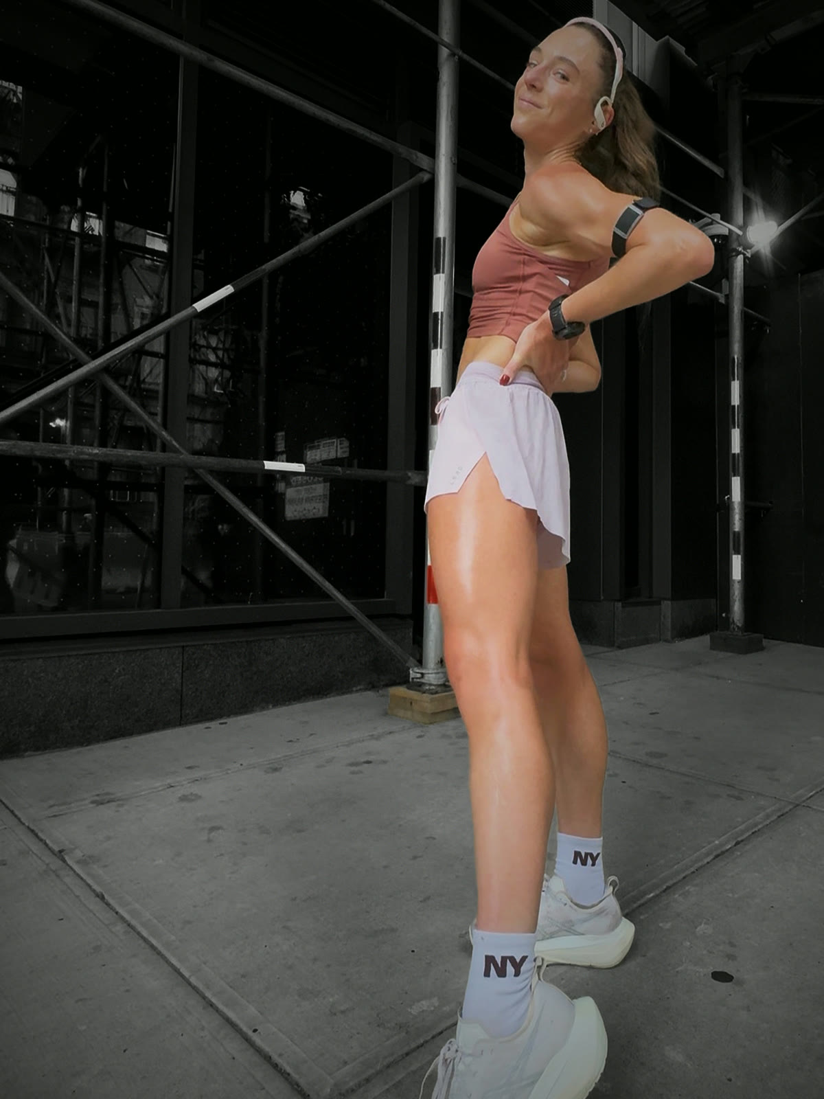 Rose Bandit crop and Marshmallow LSKD Accelerate shorts under scaffolding, ponytail down, looking back over one shoulder